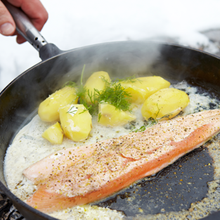 Stekpanna med röding, potatis och dill över öppen eld